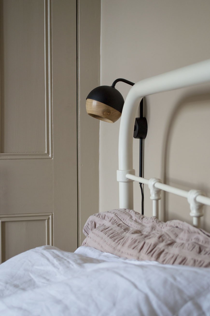 A black metal and oak bedside light on the wall in a Nordic luxe style bedroom.