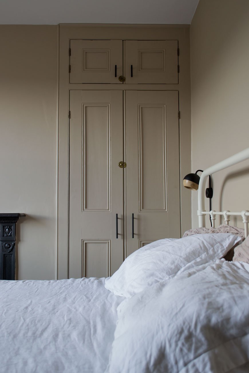 A floor to ceiling Victorian cupboard with black metal handles in a Nordic luxe bedroom