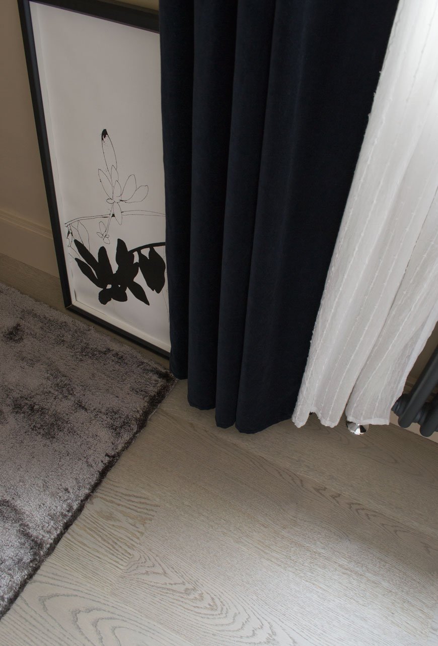 Grey oak floorboards look luxurious against the thick grey rug and velvet curtain in a Nordic luxe bedroom