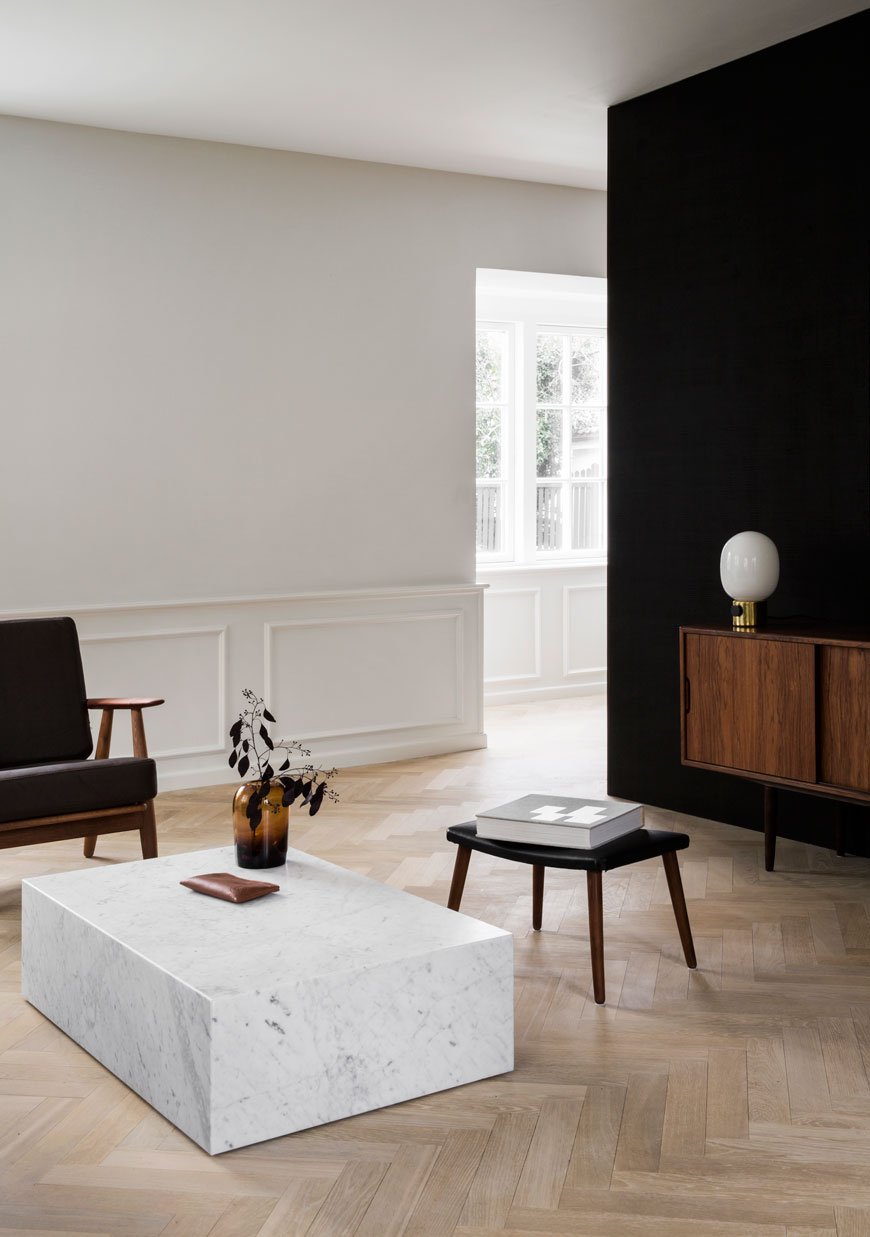 A minimalist Scandinavian living room with a marble coffee table and warm amber glass vase on top