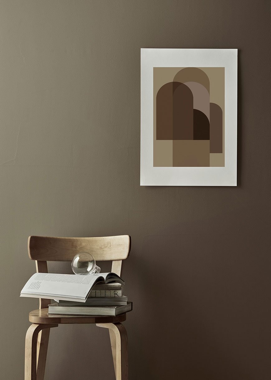 A graphic print in warm amber and rustic tones mounted on a grey green wall.