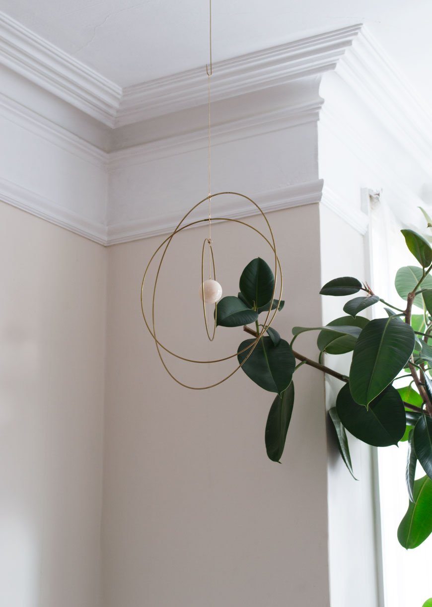 how to style your home for winter with a brass and marble mobile from NABO which hangs from the ceiling next to a tall rubber tree.