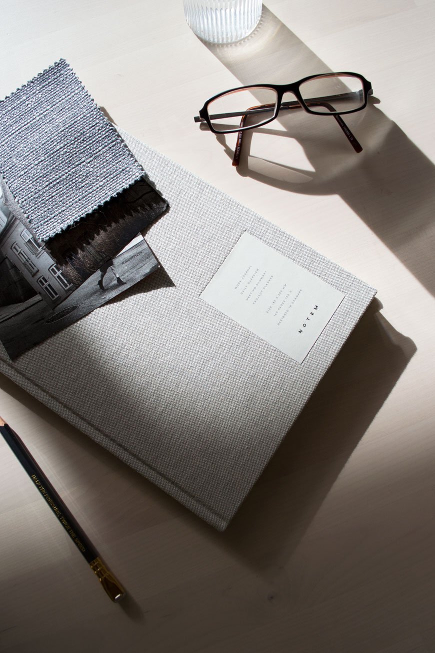 A grey cloth covered diary from NABO sitting on a desk next to a pair of glasses.