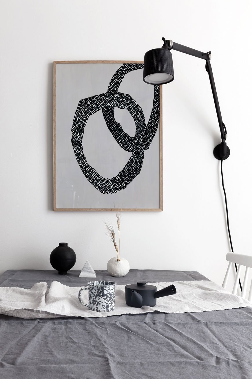 Framed monochrome abstract wall art hanging above the dining table with a black Vipp wall lamp. 