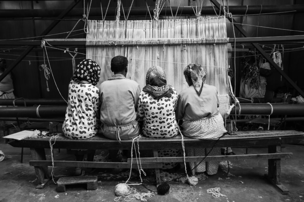 Black and white photograph of four Sera Helsinki weavers sitting at a loom together.