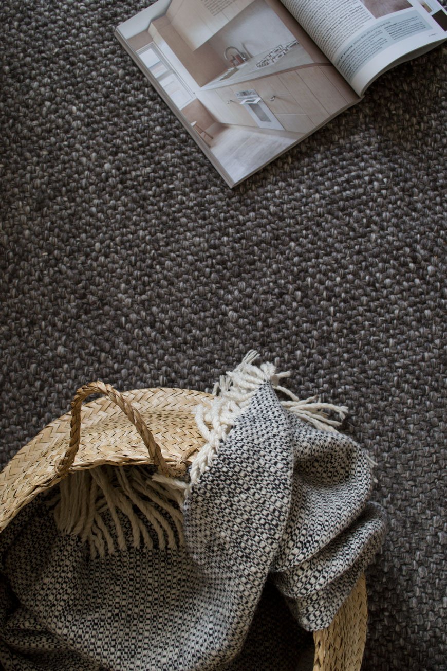 looking down onto grey wool flooring, with a basket on top of a timeless rug from British heritage brand Habitat.