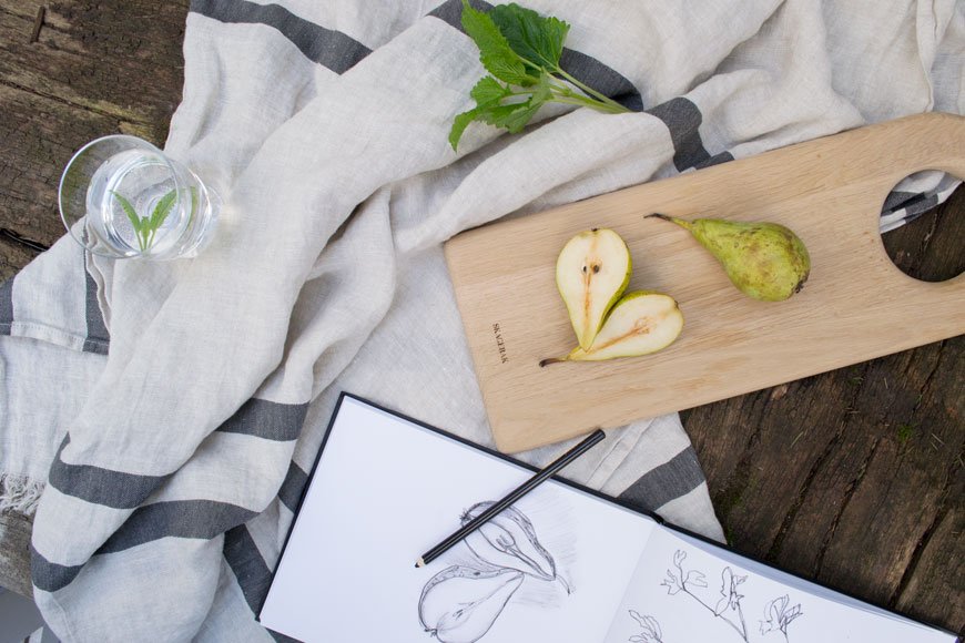 A fresh, summery still life with pears, a sketch book and a linen towel. 
