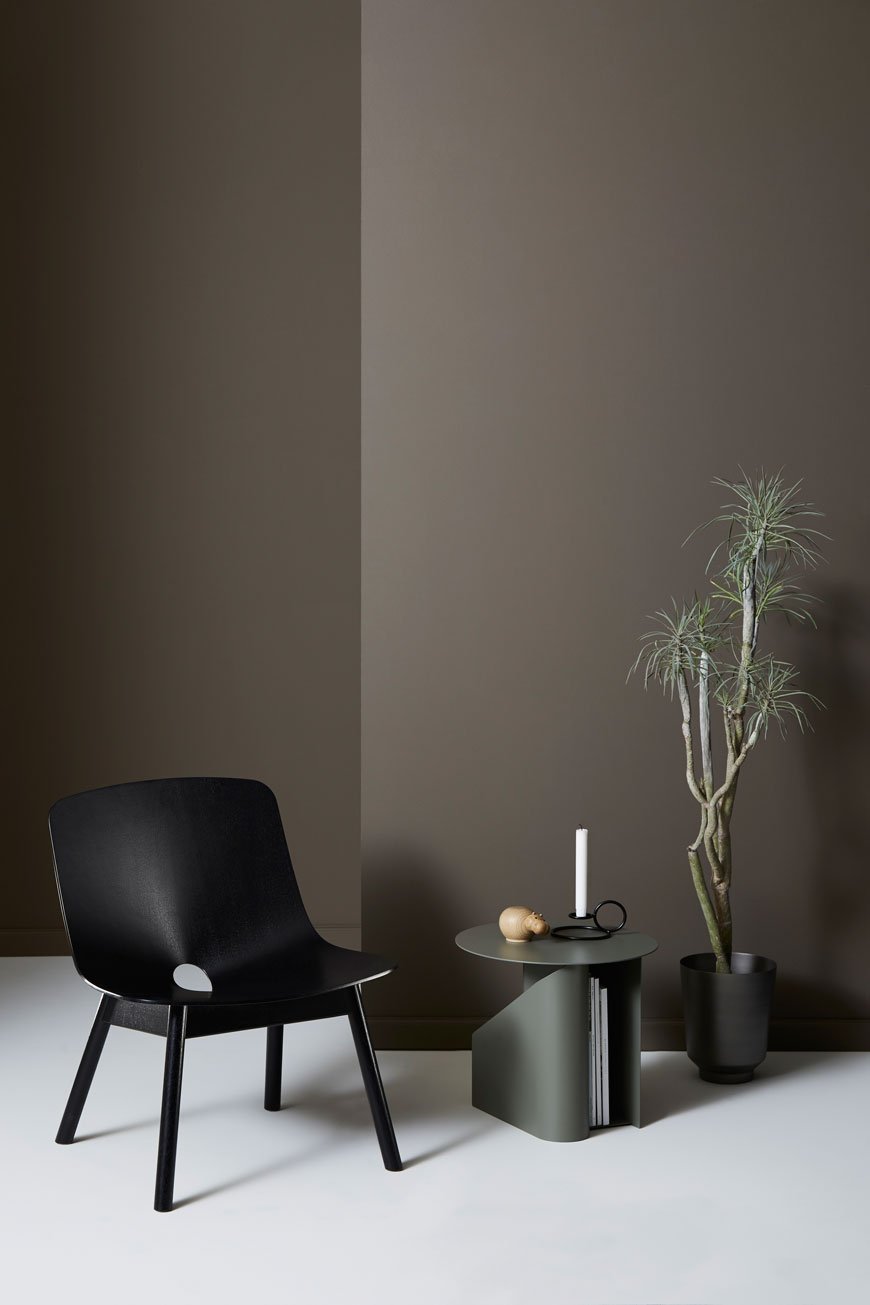 Dark and moody minimalist styling with a black ash lounge chair and dark brown walls, designed for Woud.
