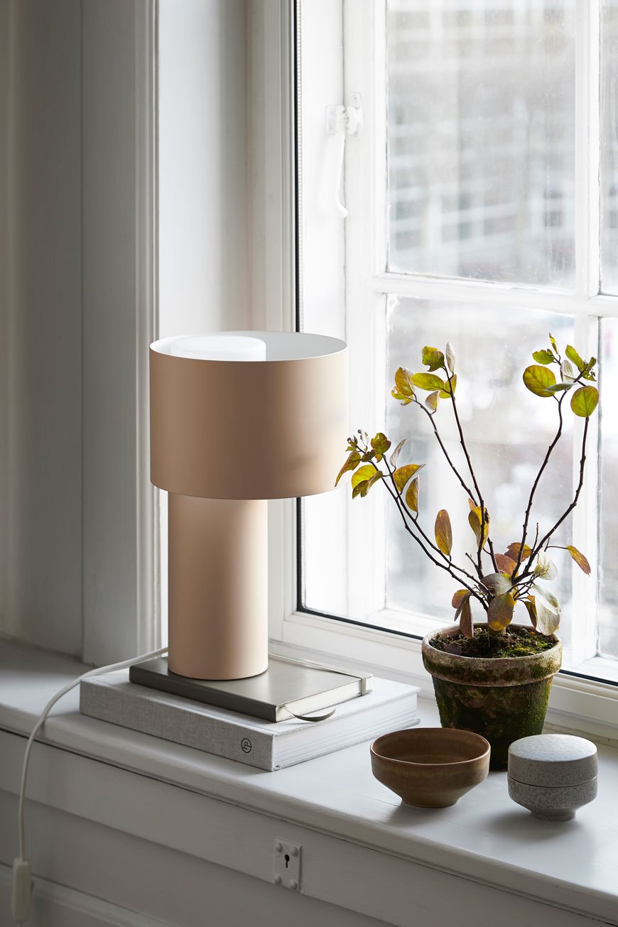 Soothing tones of the Tangent lamp styled on a windowsill with a stack of books, designed for Woud.