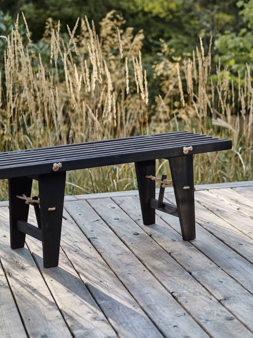 Oiled black slatted wooden bench, a striking example of contemporary outdoor furniture in a prairie garden.