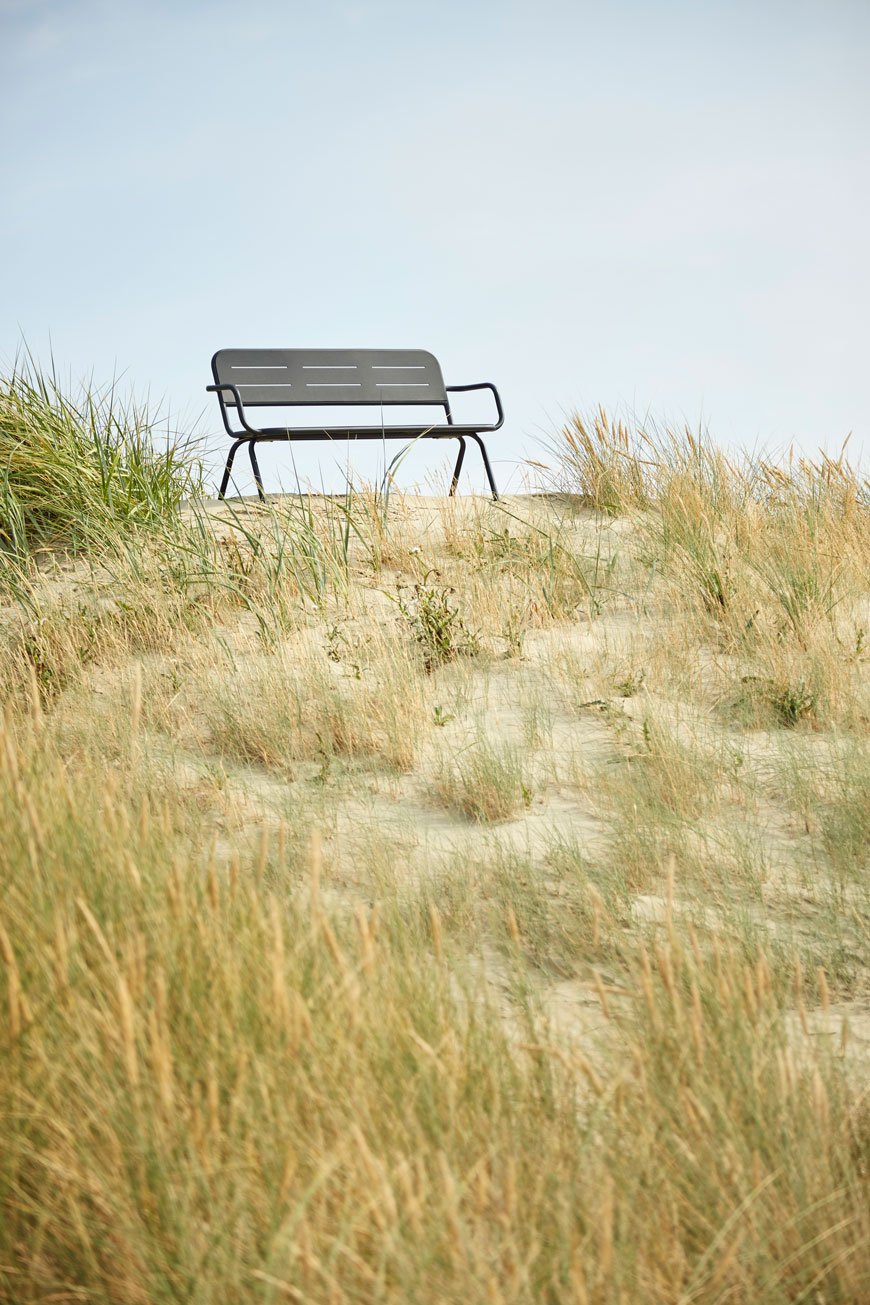 A black metal bench sitting on top of a grass dune, a perfect example of Modern Scandi outdoor furniture.