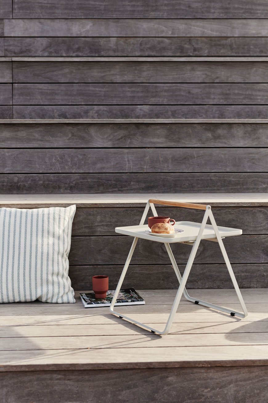 A white metal side table used as outdoor furniture on a wooden desk with striped cushion. 