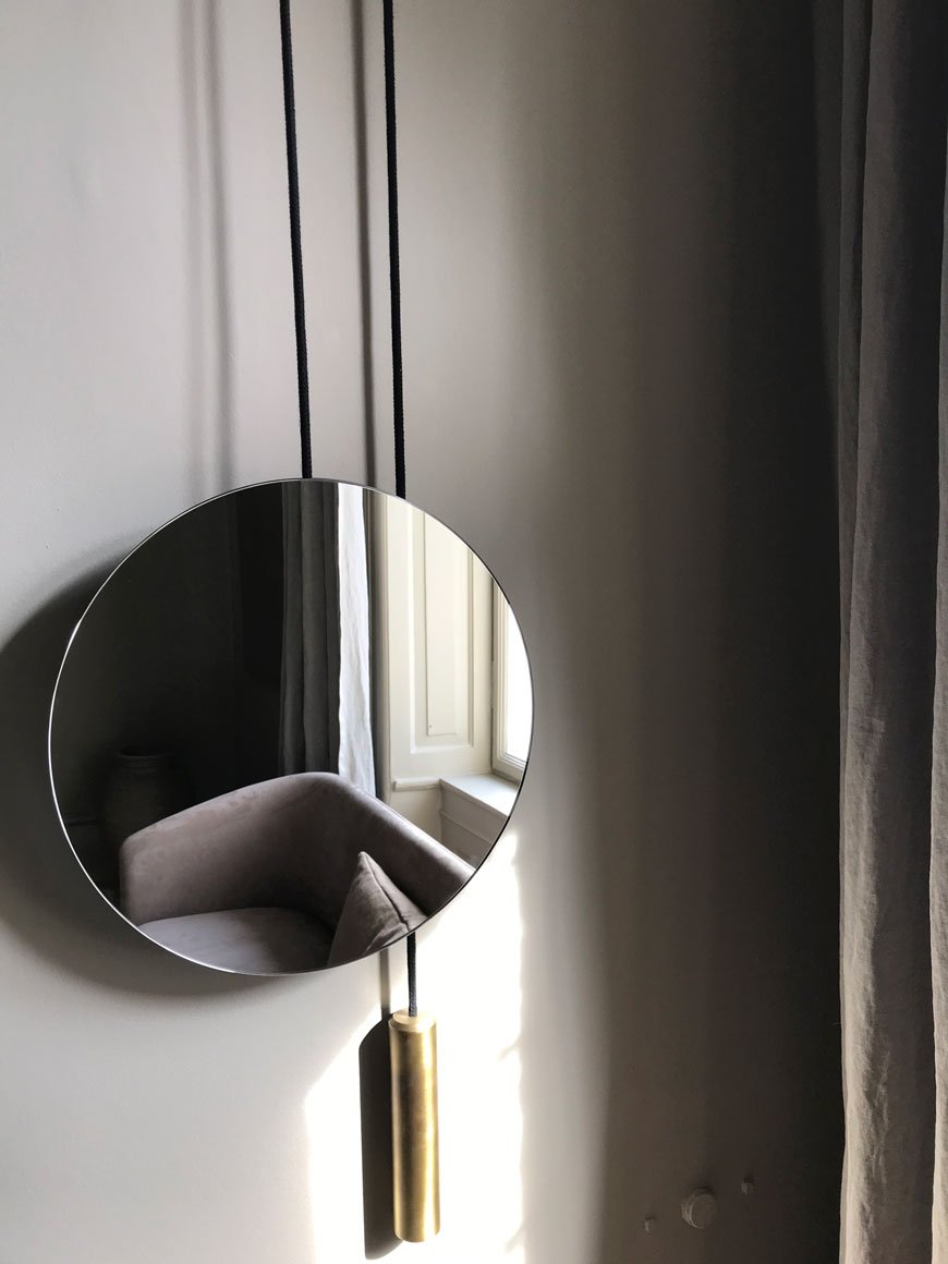 Round mirror with brass rope detail reflects back a grey chair in the New Works showroom.