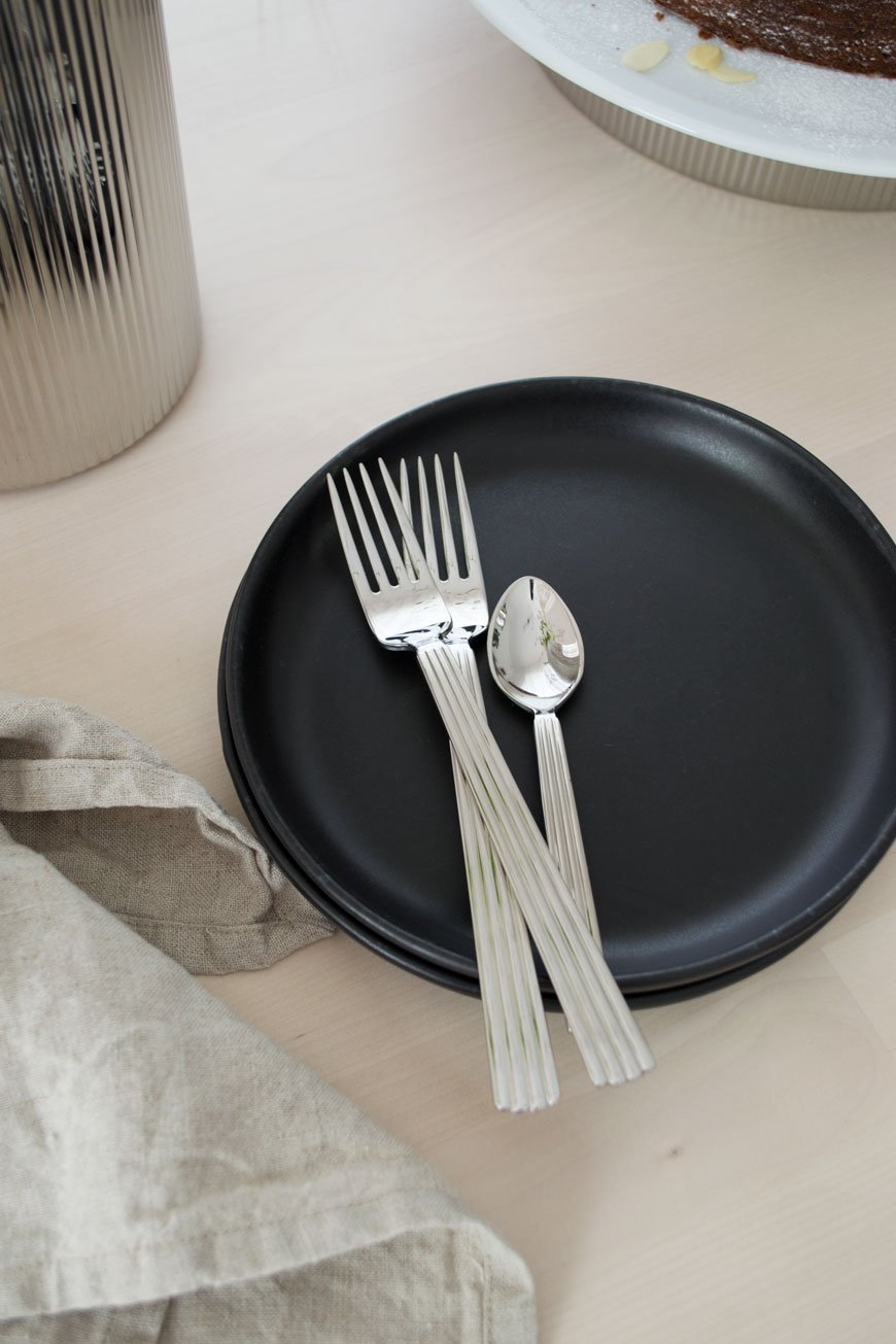 Modern, stylish cutlery from the Georg Jensen collection sitting on a stack of black side plates.