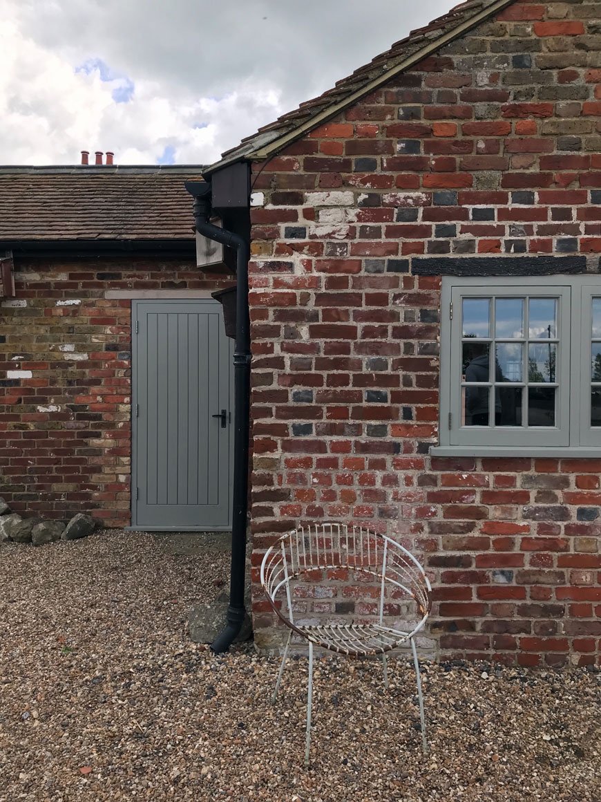 An old brick outhouse with grey green painted door and window at Elmley in Kent.