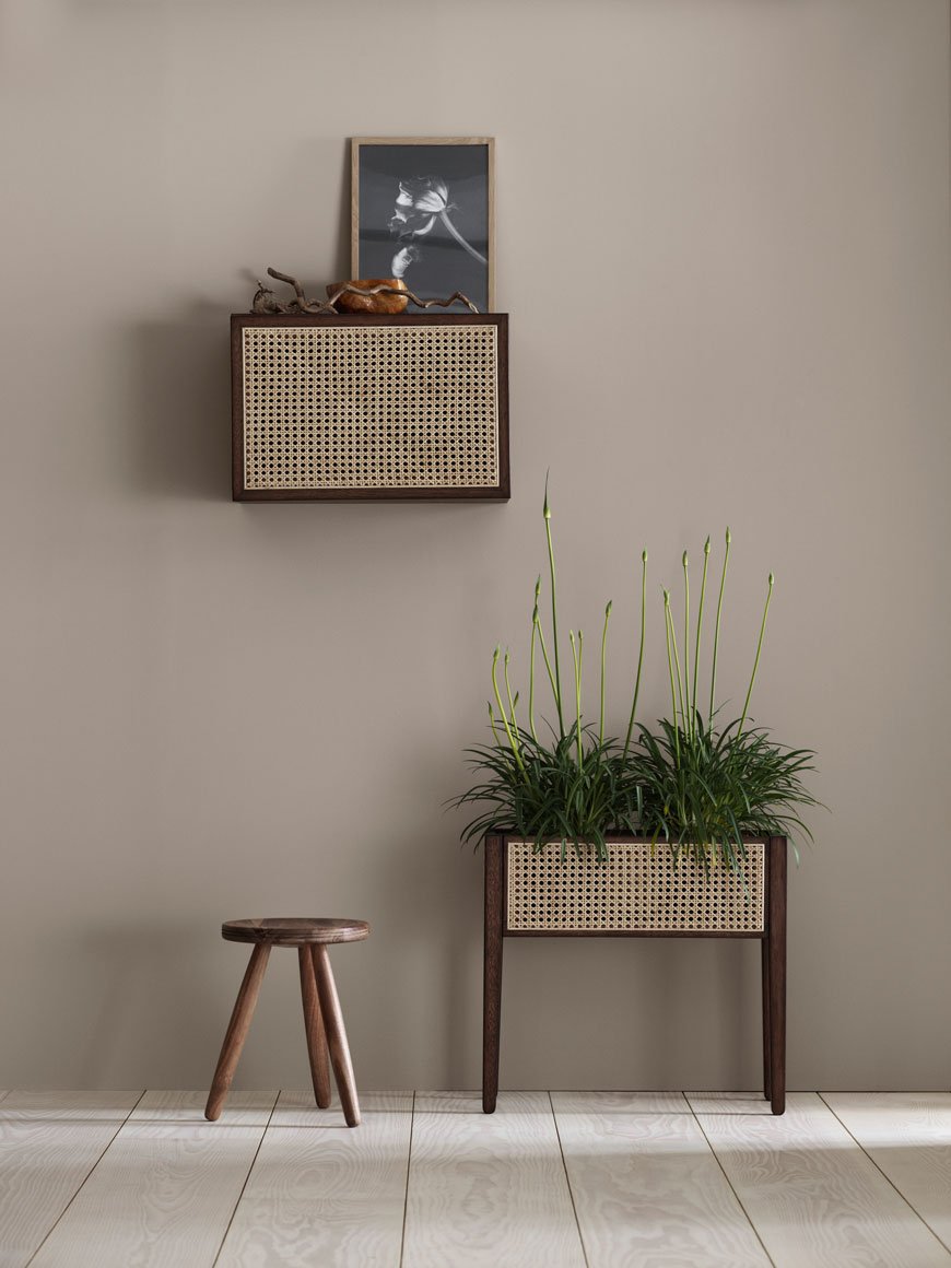 Dark wood and rattan storage cabinet and planter styled in a light beige hallway.