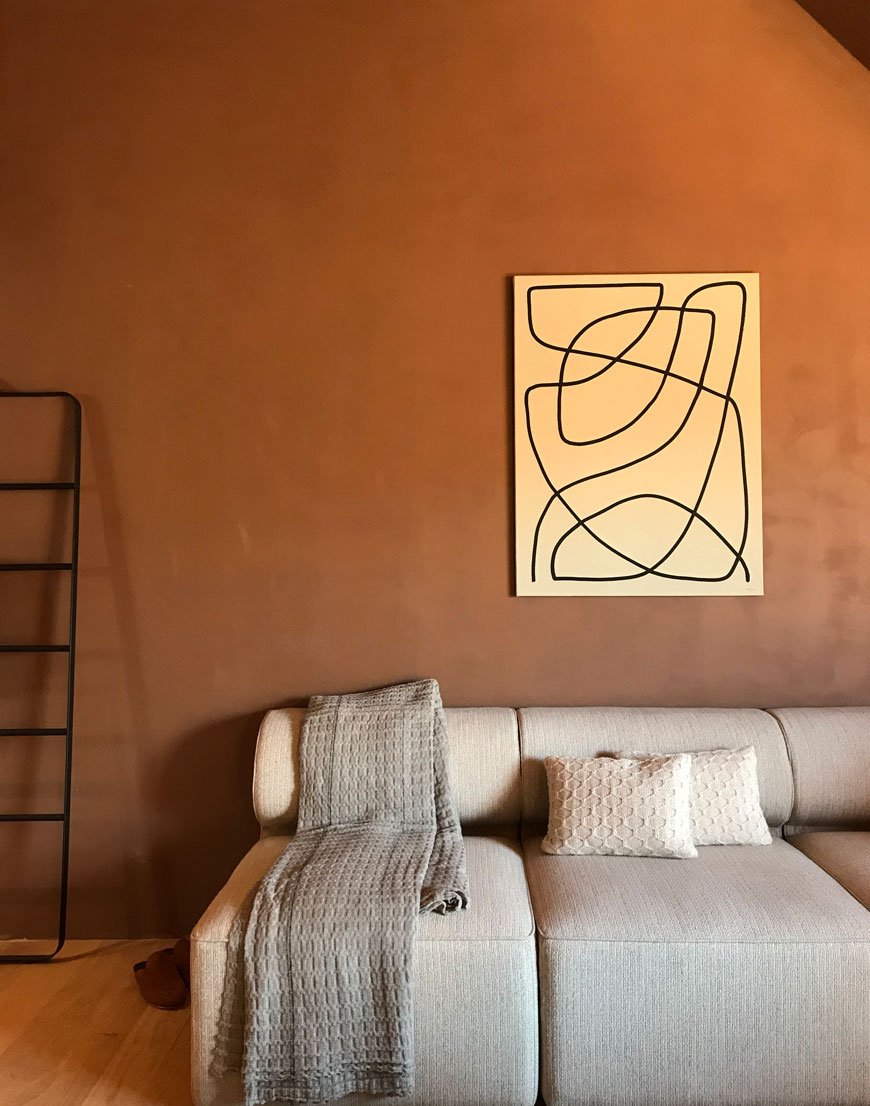 Rich and earthy walls set off an abstract piece of art inside the Studio suite at The Audo, a new hybrid hotel and creative residence in Copenhagen. 
