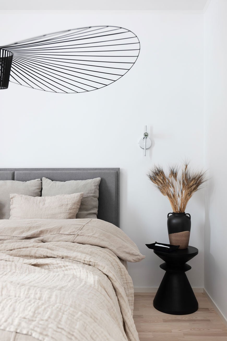 A minimal, neutral Nordic bedroom with linen bedding and a vase of grasses. 