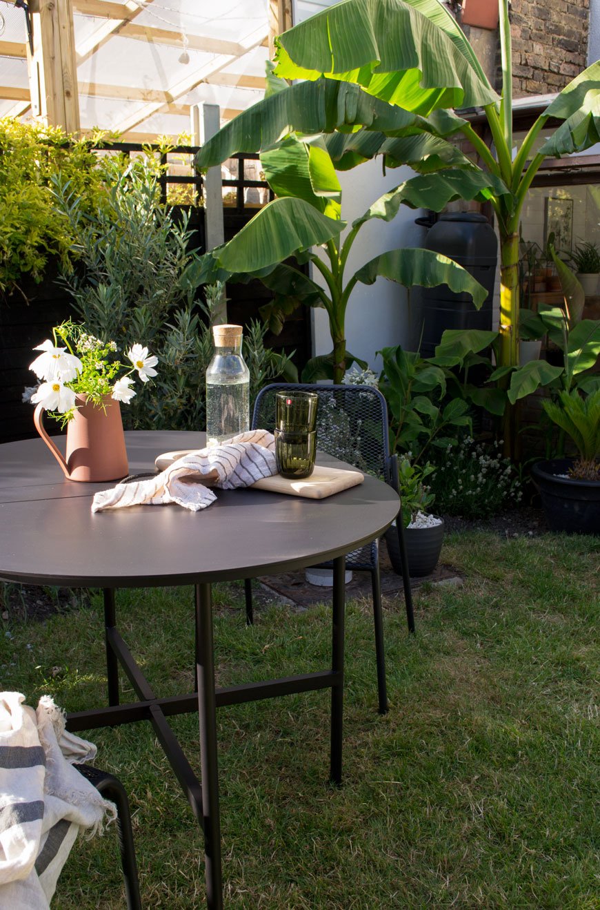A stylish table and chairs in front of tropical banana trees shows how to make the garden feel like an extension of your home. 