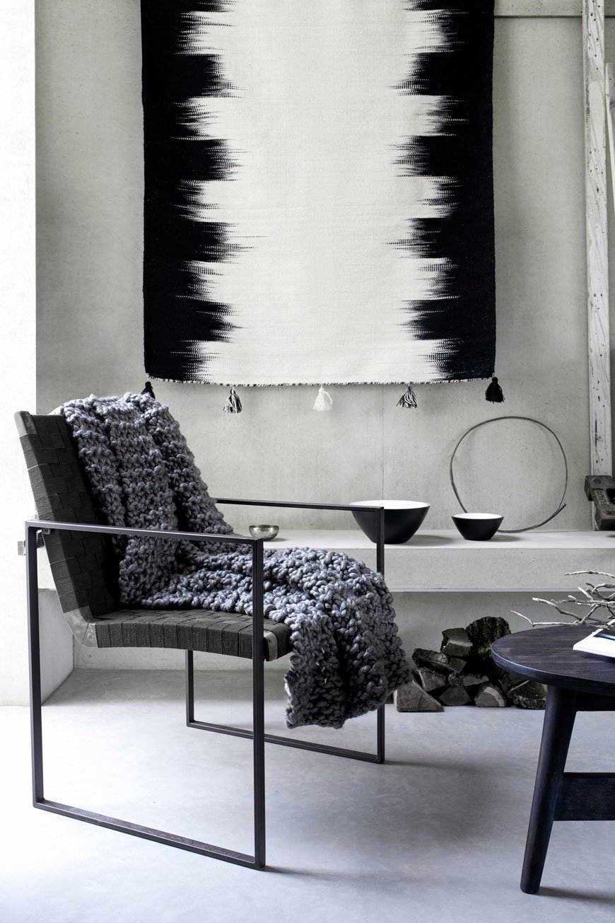 Striking black metal armchair in a modern concrete living space. styled with a grey chunky knit blanket. 