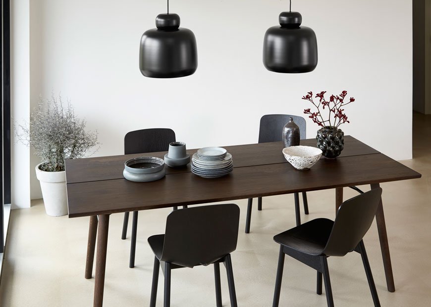 Dark smoked oaked Alley dining table designed by Woud set for entertaining paired with black pendant lights and black chairs. 
