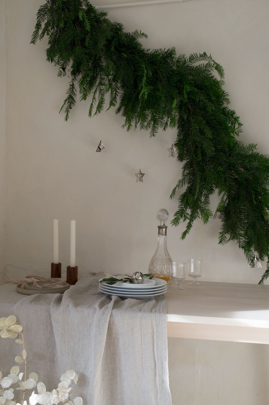 A Nordic Christmas table styled with a linen tablecloth, yew tree garland and Georg Jensen's Christmas Collectibles for 2019. 