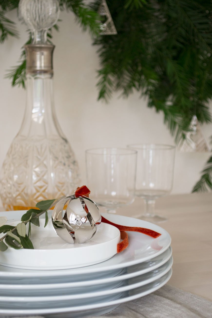A sweet Ball Ornament styled on top of a stack of white dinner plate on the Christmas table. 