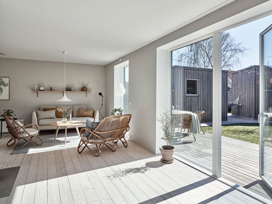 A stunning open plan L-shaped wood clad island home painted in light grey with minimal Scandinavian furniture.