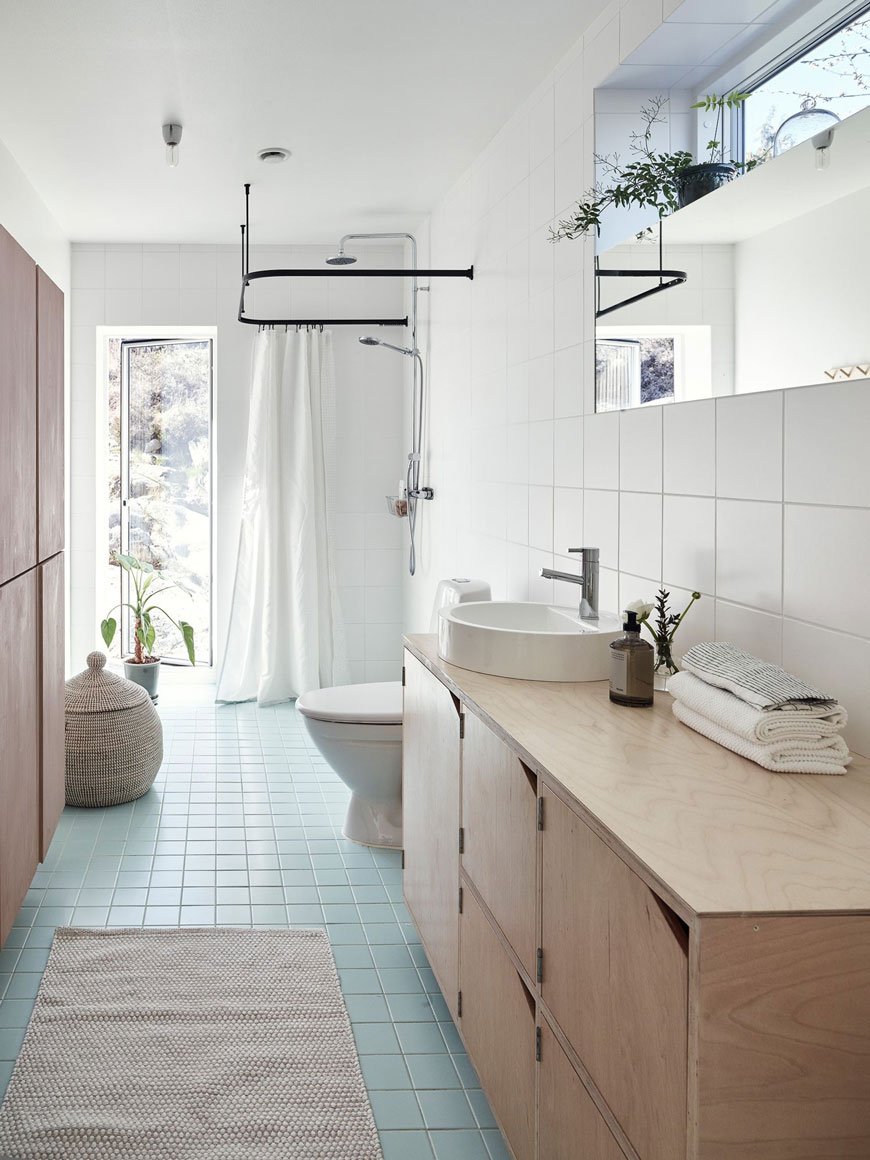 A bright, white tiled family bathroom with a square turquoise tiled floor and black hanging shower rail. 