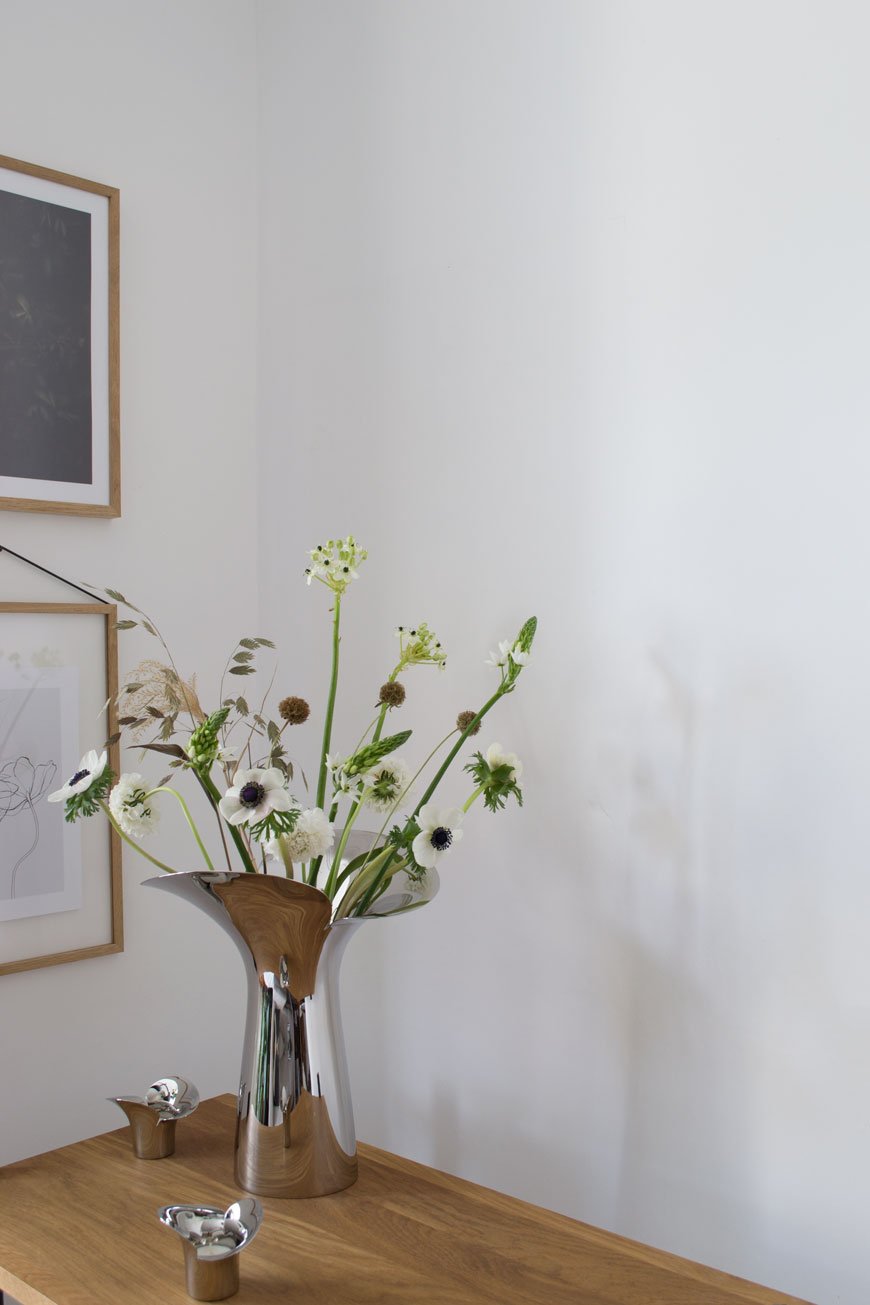 The poetic and sculptural Bloom Botanica vase collection by Georg Jensen typifies the elegance of timeless Scandinavian design, styled with white spring flowers in a minimal white living room. 
