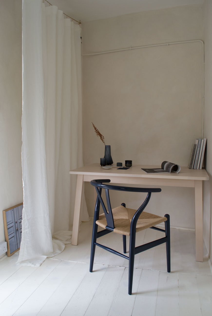 A warm, minimalist home office with limewashed walls and an inky blue Hans J. Wegner Wishbone chair. 