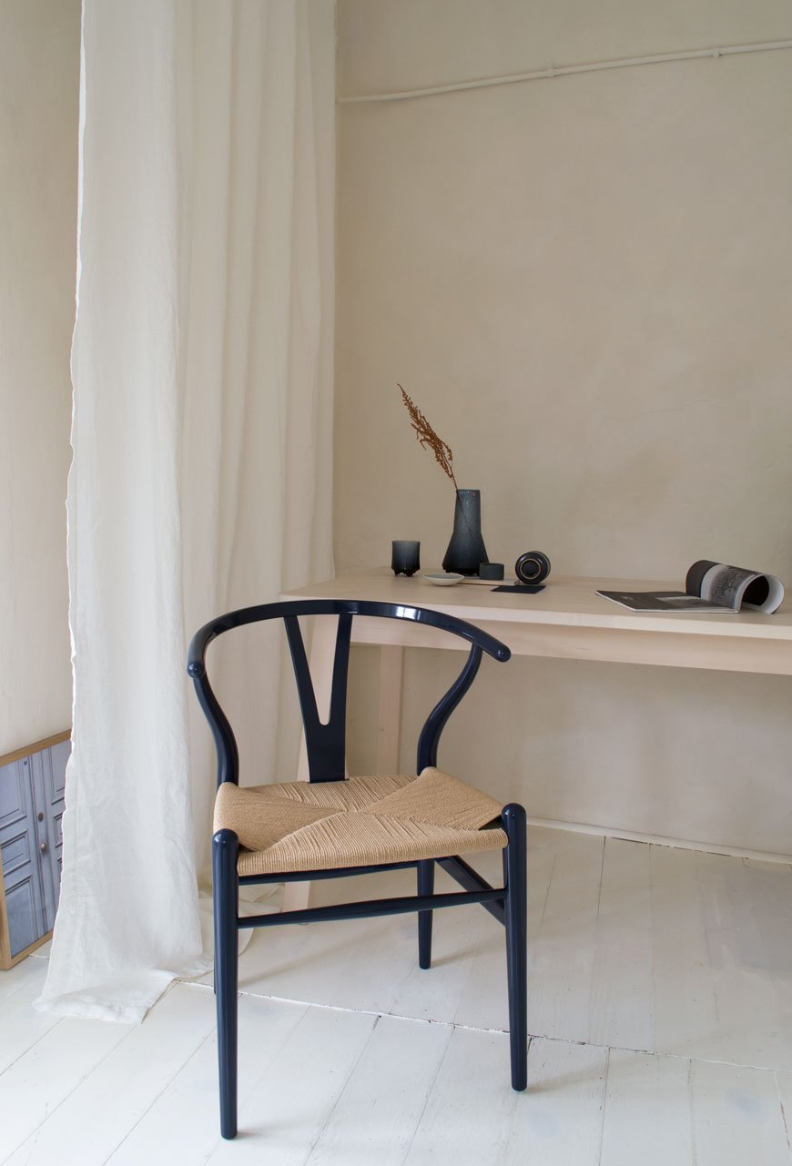 A pale and moody home workspace with limewashed walls and white painted floorboards with the 2020 limited edition CH24 Wishbone chair in navy blue. 