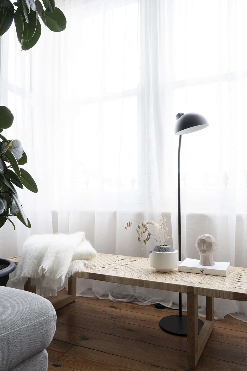 A minimal Nordic living room in neutral tones with a black floor lamp and rattan table bench from Carl Hansen & Son. 