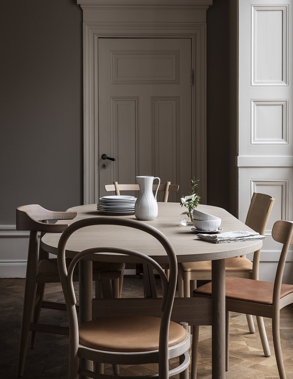 A moody Scandinavian dining room at the Gärsnäs apartment with an extendable pale oak dining table and mis-matched dining chairs. 