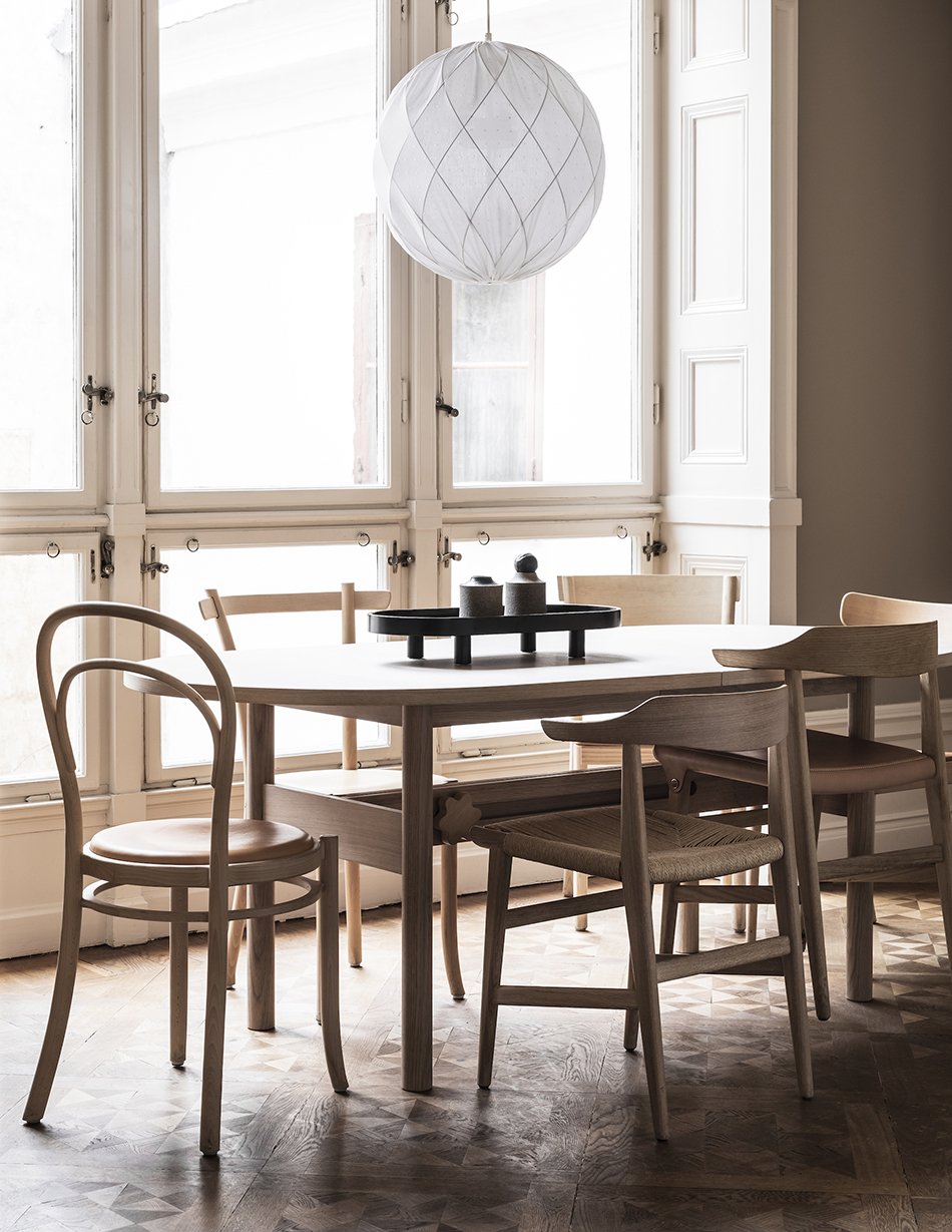 A light beige dining room with a long oak dining table and mix of pale oak and leather dining chairs. 