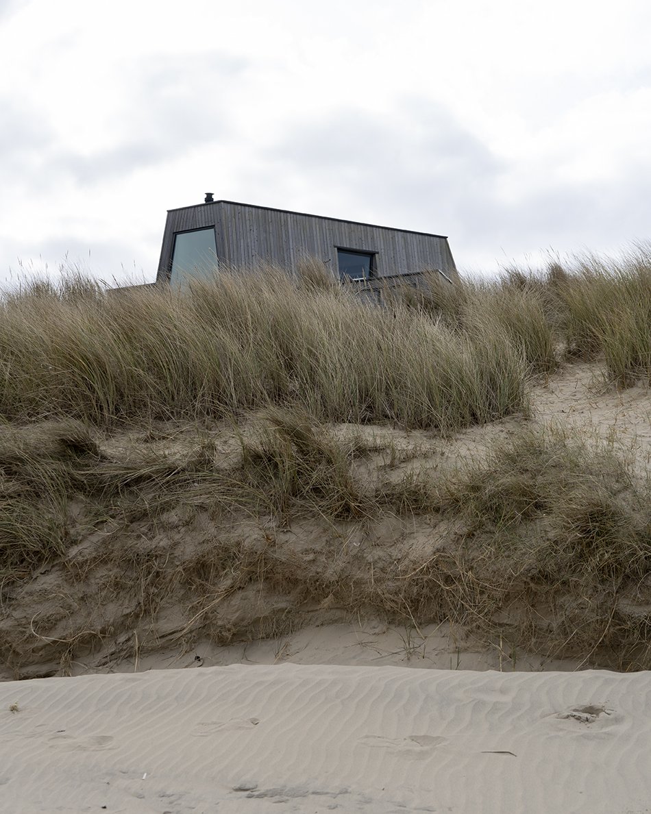 A contemporary beach house clad in larch wood with large windows on the grassy dunes of sandy beach at Greatstone, Kent. 