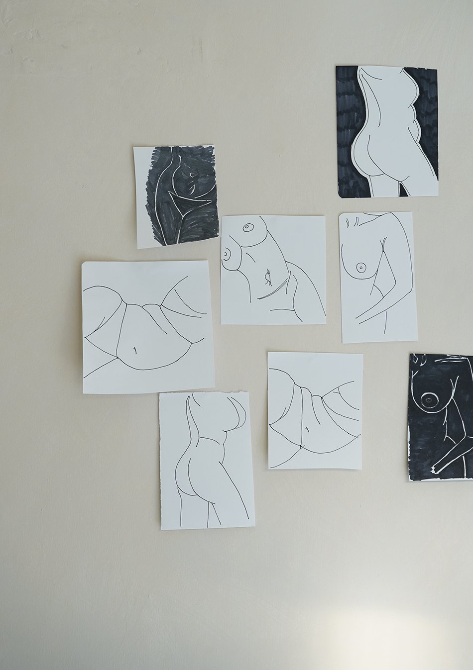 A collection of abstract female body line drawings in black pen on a wall. 