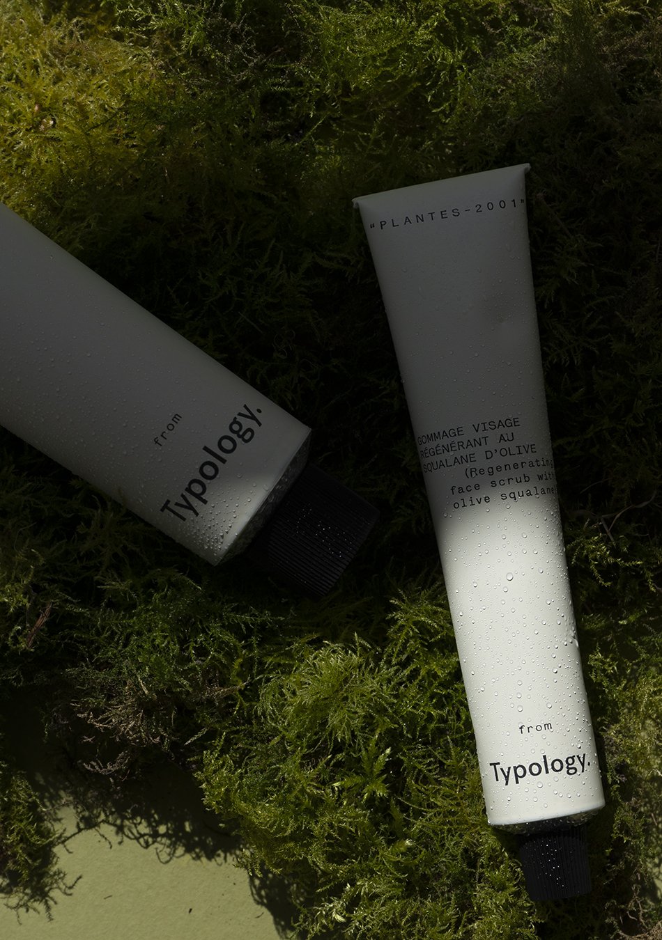 New minimal skincare body scrubs from Typology, styled in strong shadow on a bed of moss. 