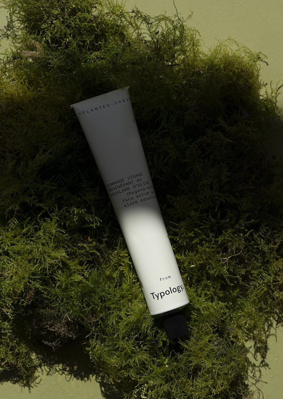 New tube of face scrub with olive squalane from Paris based minimal skincare brand Typology on a bed of green moss. 