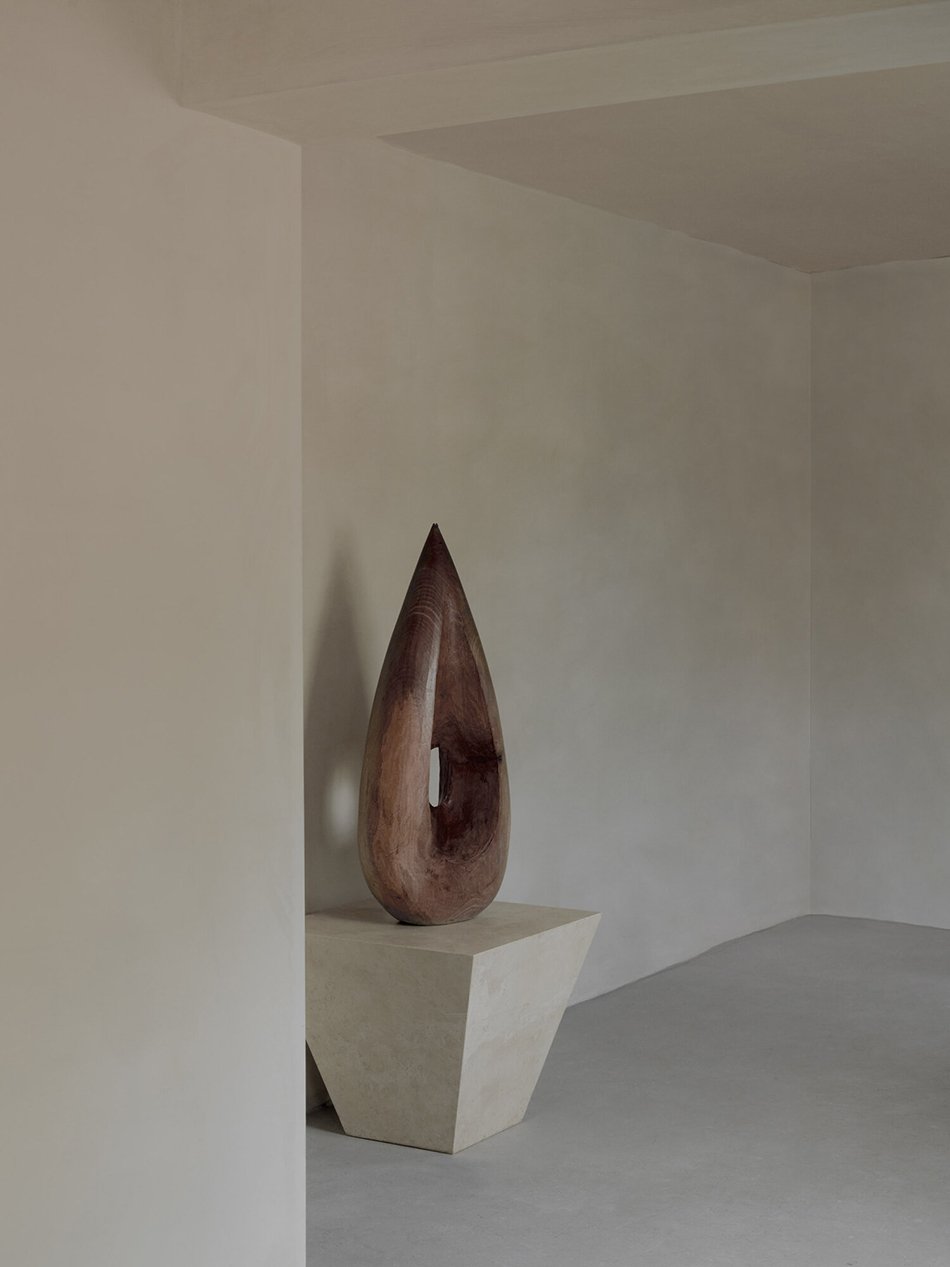 A carved contemporary wooden sculpture in a minimal space painted with pale beige textured lime paint. 