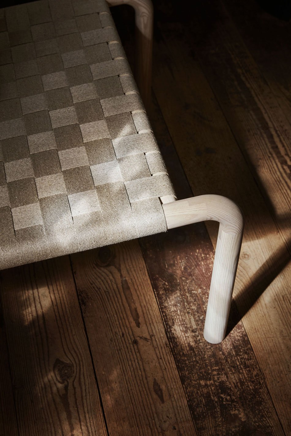A close-up detail shot of the natural linen woven seat and curved leg join of the Kaski lounge chair. 