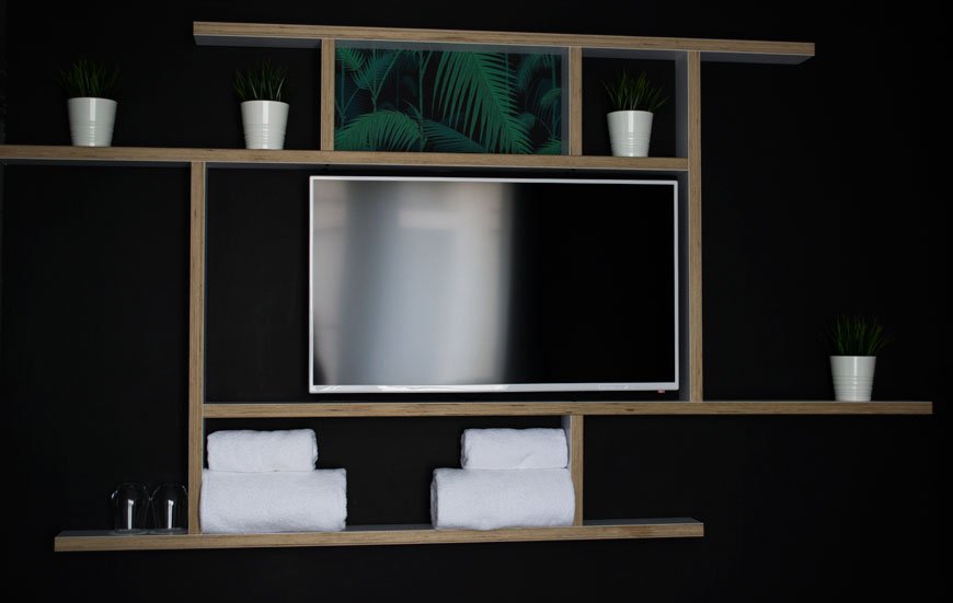 Dark painted wall with stylish shelving and mounted TV at Kip hotel, London
