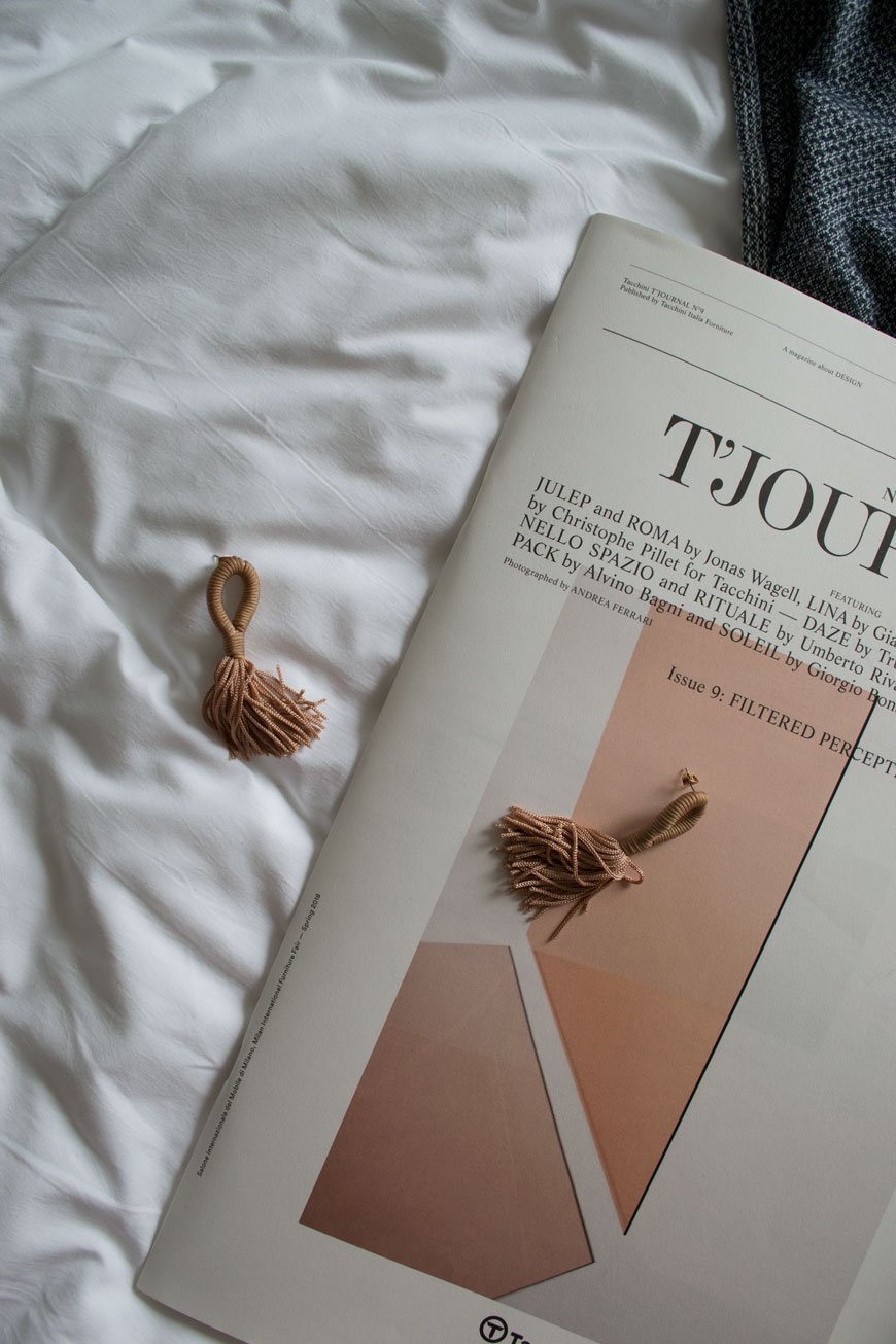 Lifestyle shot of a newspaper and tassel earrings on the bed at The Good Hotel London, 