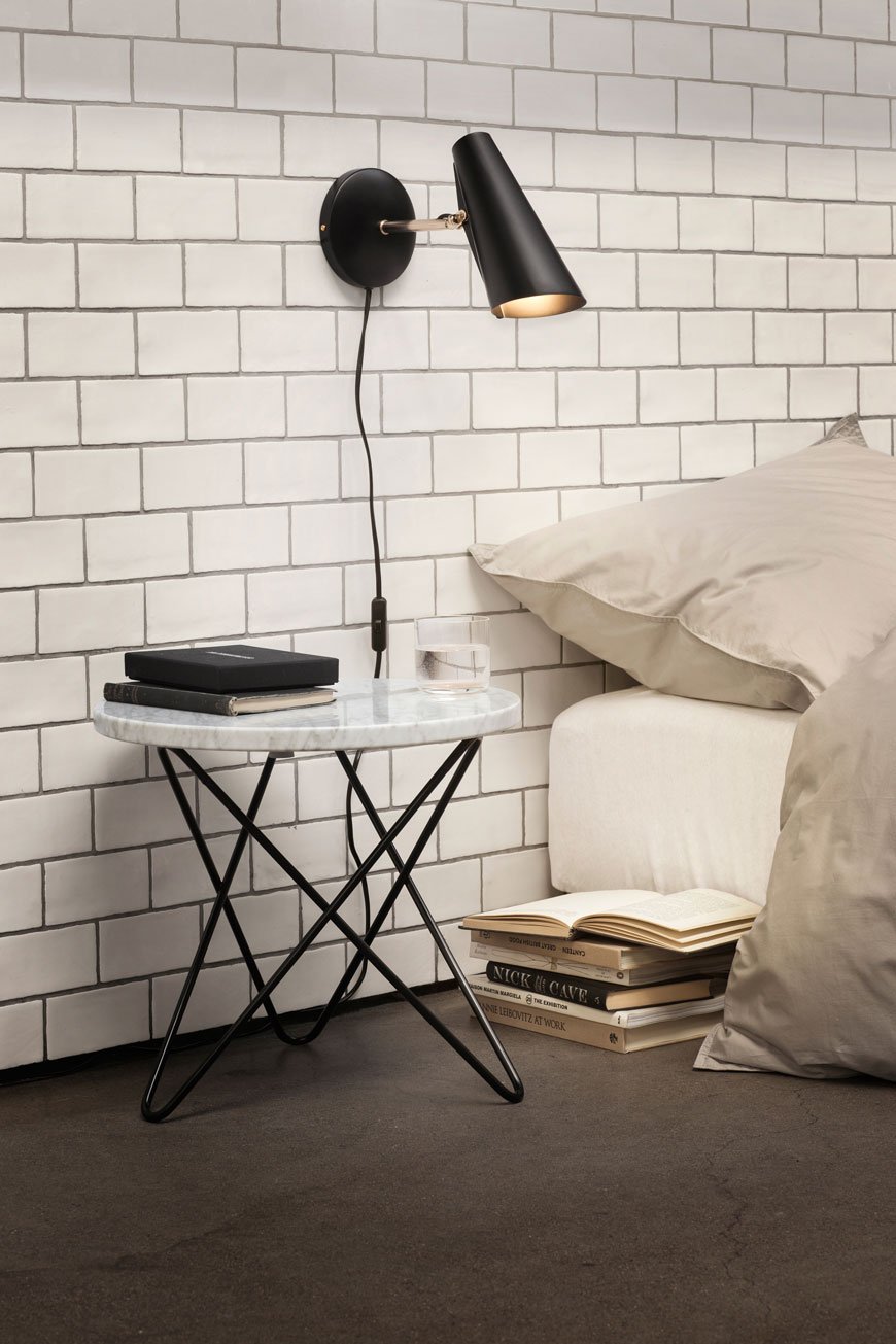 black wall light on white tiled wall with marble bedside table in a minimal bedroom