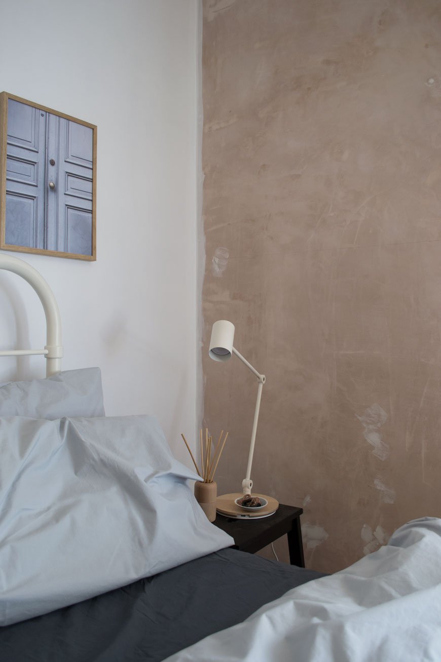 A white bedside lamp in a bedroom with light and dark grey cotton sheets on the bed