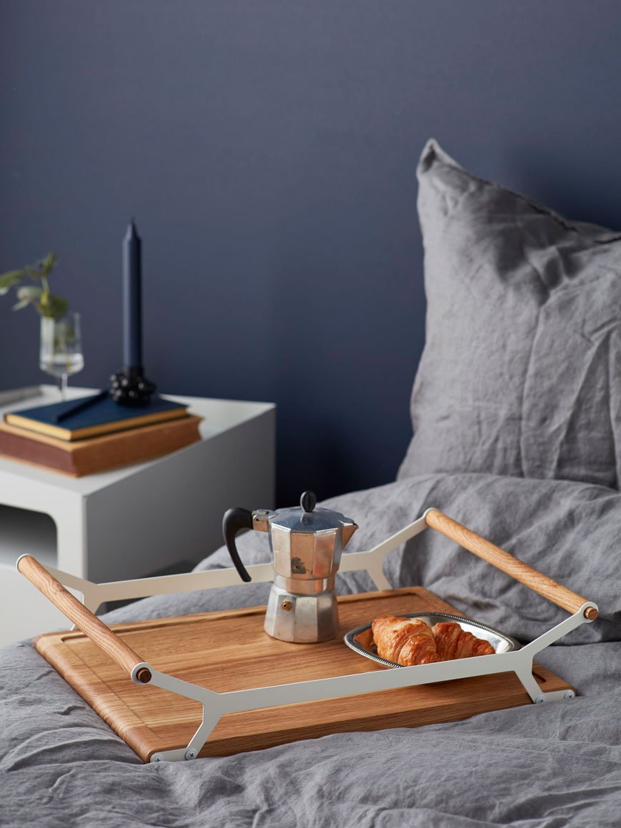 Breakfast in bed with a wooden tray in a cosy blue bedroom, by Nordic design brand Gejst