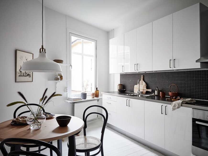 A black and white monochrome kitchen in Gothenburg with a small round table and black Thonet cane chairs and black mosaic splashback.