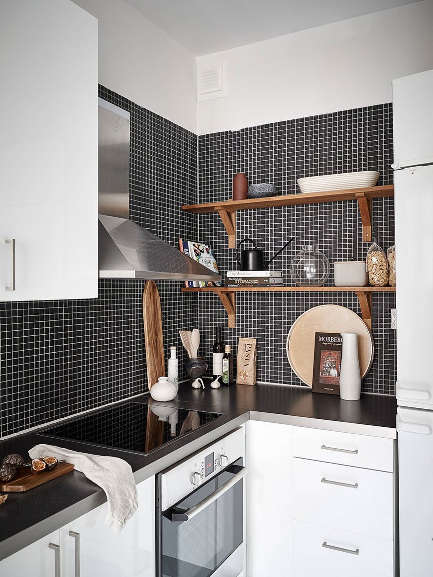 Black mosaic tiled wall in a monochrome kitchen with open wooden shelves, high gloss white units and bags of pasta