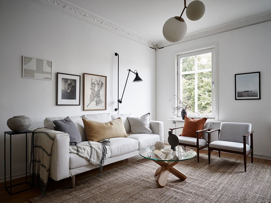 White living room with white sofa, rattan rug and two grey Mid-Century chairs in an apartment