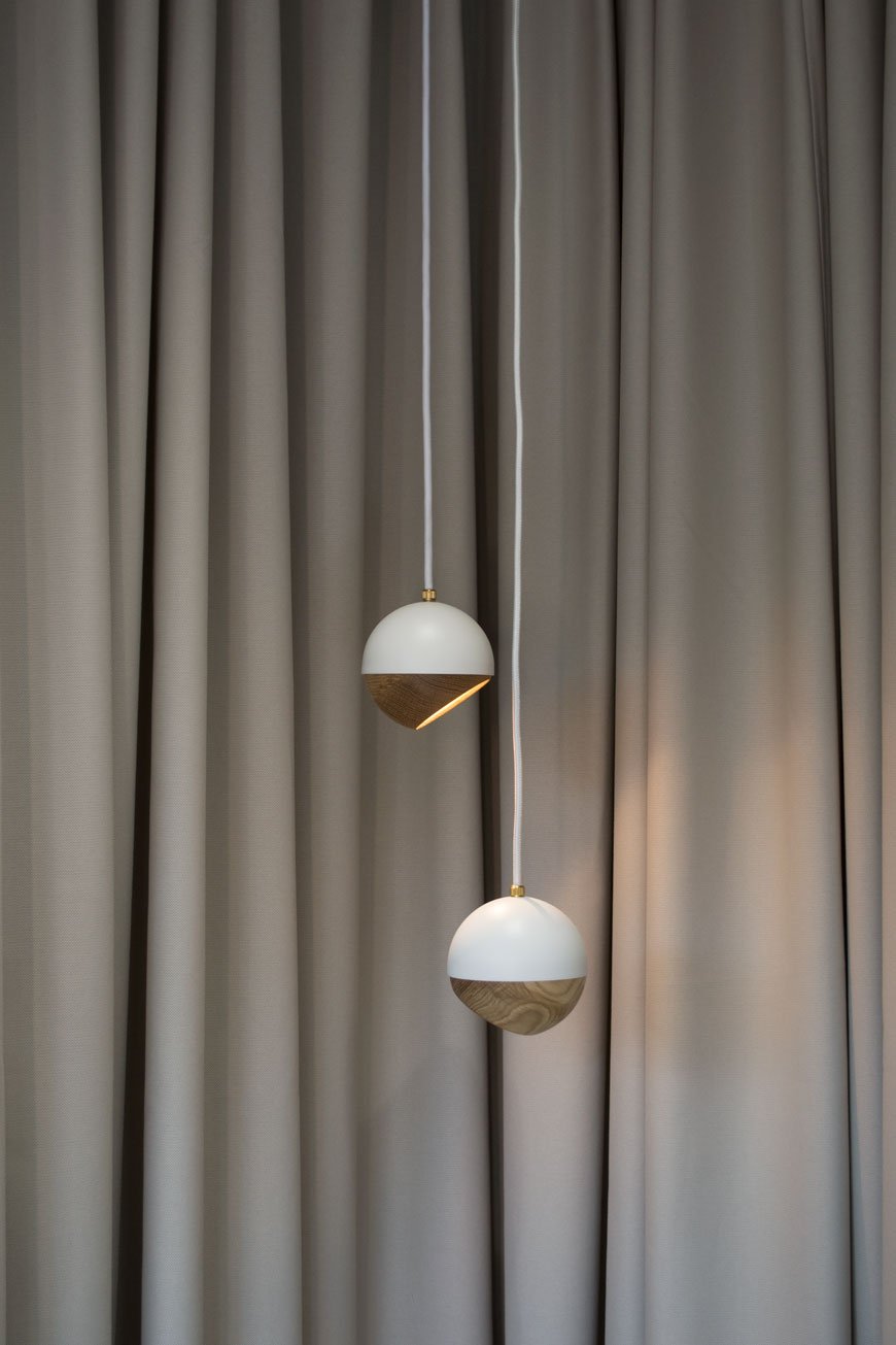 Two white and oak Ray pendant lamps against a grey curtain at Mater Gallery, Clerkenwell.